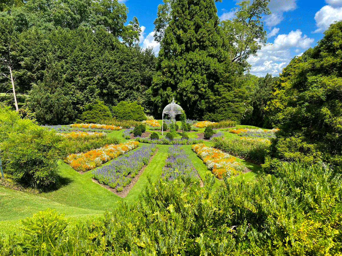 A garden at Hills & Dales Estate in LaGrange, Georgia, blooming with vibrant garden flowers and lush trees and bushes.