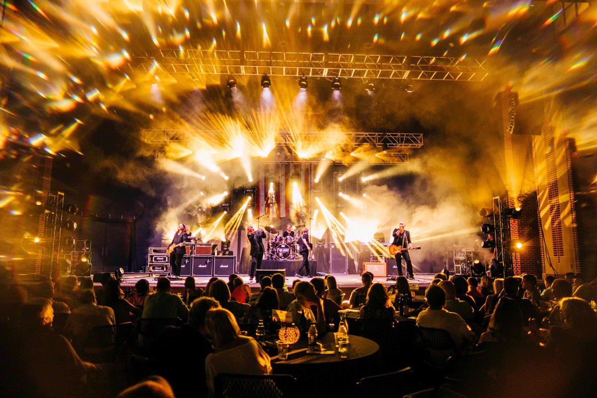Bright yellow concert lights streaming out from the stage with a crowd below at Sweetland Amphitheatre in LaGrange, Georgia.