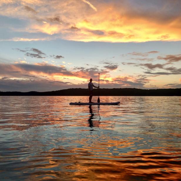 person paddle boards on the lake at sunrise or sunset