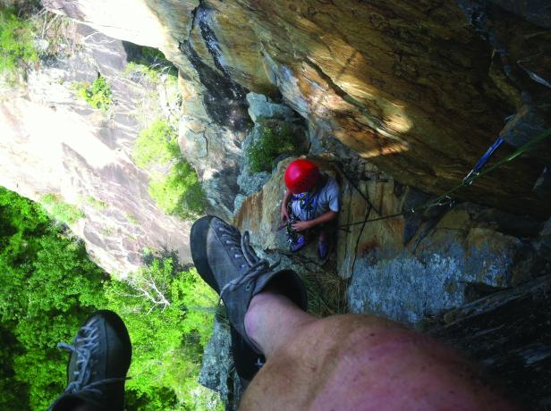 camera points down at person fixing rock climbing gear from higher on the gorge