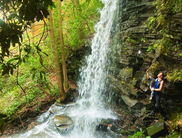 woman and child stand under waterfall looking up