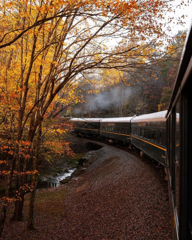 A train runs along the tracks through colorful fall foliage