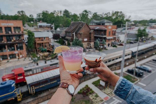 Two hands holding cocktails on the roof at Hook & Eye in Blue Ridge, Georgia